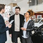 person signing car rental agreement with keys and vehicle in background