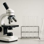 A laboratory microscope with test tubes and a flask on a table